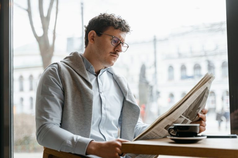 Adult man reads a newspaper by a café window, enjoying a coffee break indoors. — Realz Casino: Schnelle und sichere Zahlungsm