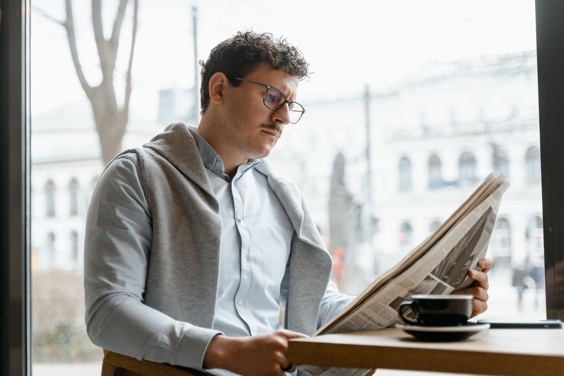 Adult man reads a newspaper by a café window, enjoying a coffee break indoors. — Realz Casino: Schnelle und sichere Zahlungsm
